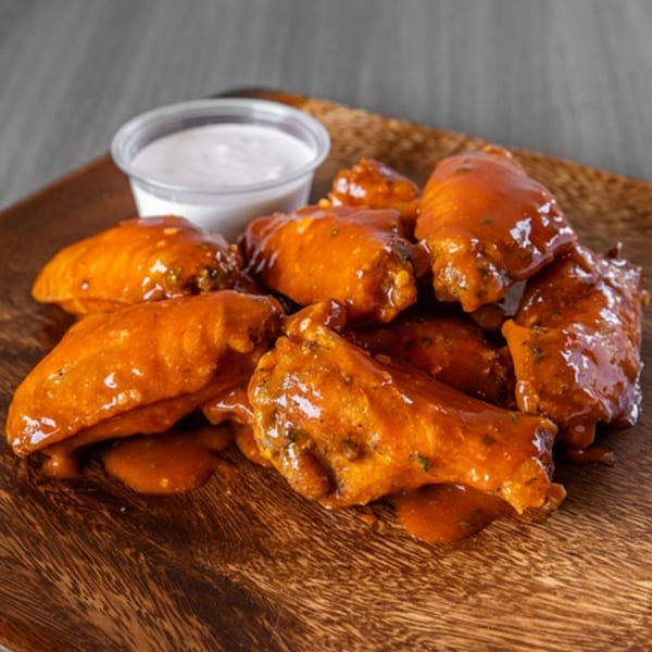 Ameci Pizza Kitchen's buffalo wings, coated in orange sauce, with a side of ranch dressing on a wooden board.