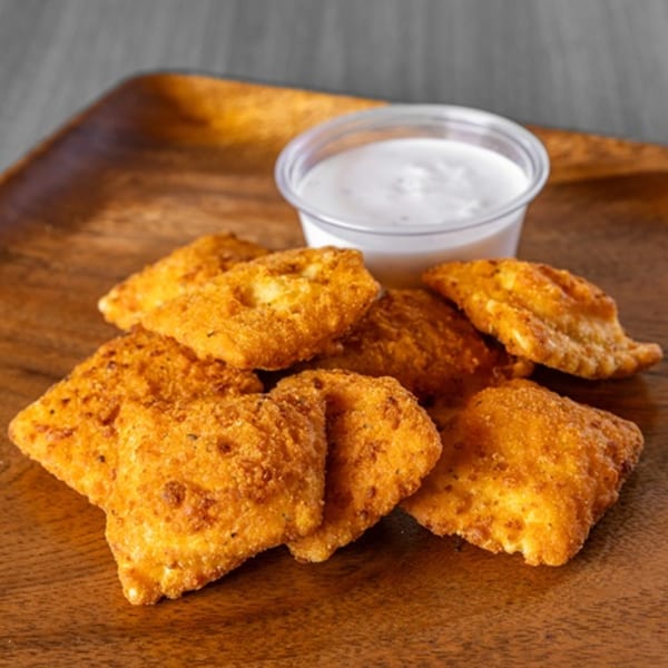 Golden-brown fried ravioli with a side of creamy white dipping sauce on a wooden tray.