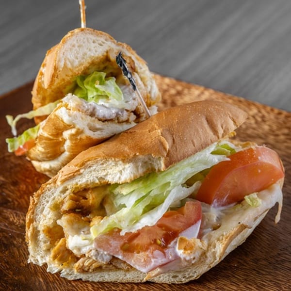 Two chicken subs with lettuce, tomatoes, and sauce on a wooden board.