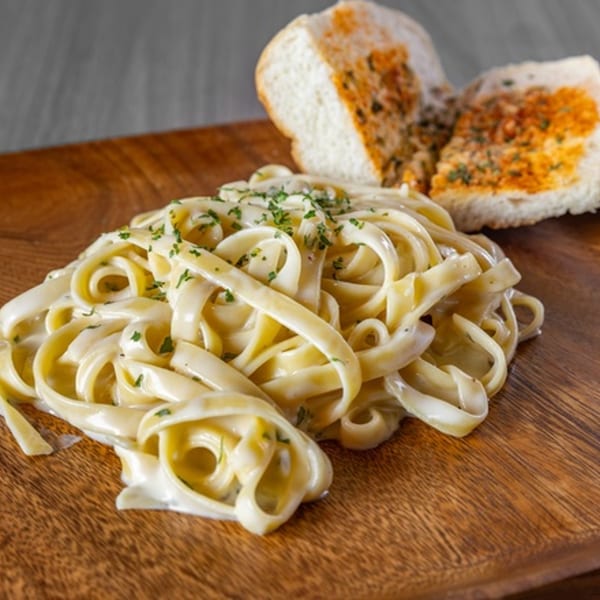 Fettuccine Alfredo pasta with parsley and two slices of garlic bread on a wooden board.
